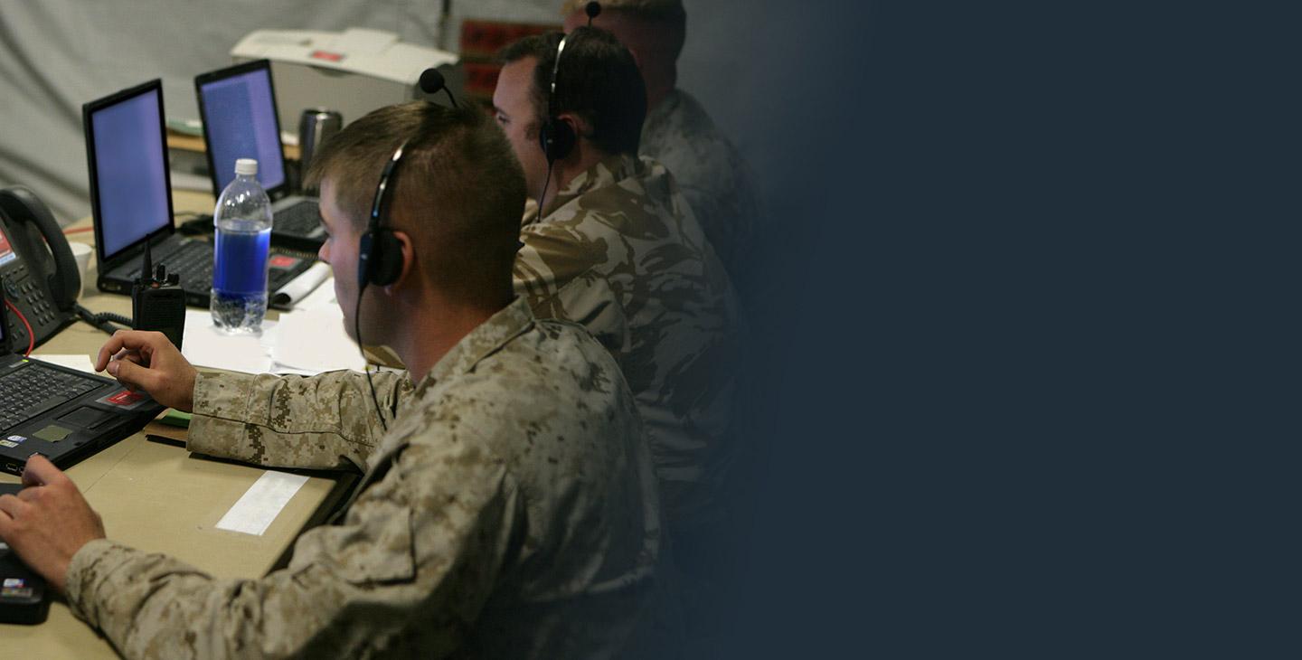 Three male warfighters looking at a laptop in a tactical operations center